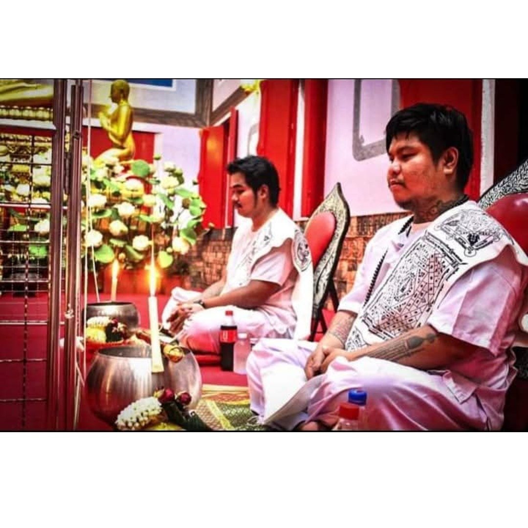 Two ritual practitioners seated before a temple altar during an amulet consecration ceremony.