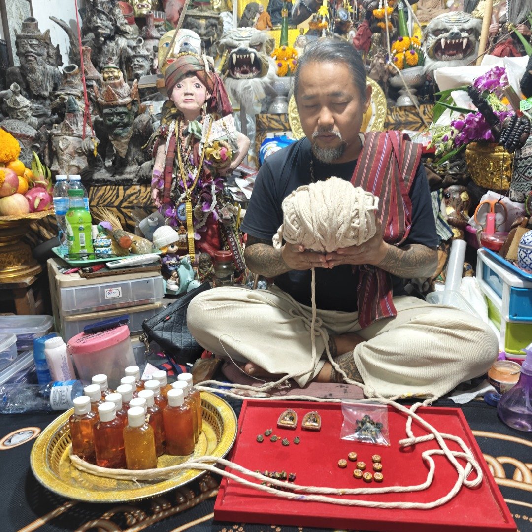 Ajarn Wanchai performing the consecration ritual for the Khun Chang wealth amulet batch, estimated BE 2554, surrounded by ritual materials and sacred objects.