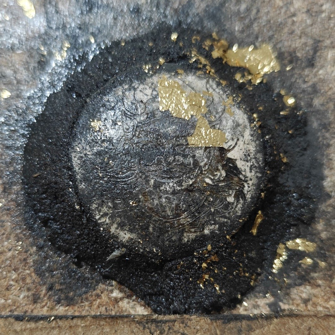 Close-up of the specially selected prai panneng engraved with Phaya Yom, surrounded by cremation sludge and gold leaf.