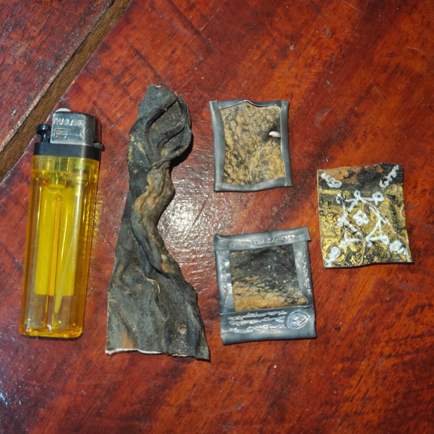Prai John Wicca by Ajarn Kitkamo BE 2569, showing several uncased ritual pieces with yant markings beside a lighter for size comparison.