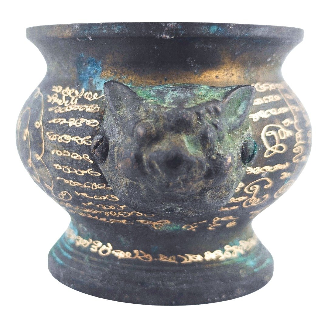 Close-up of an animal-head handle with green patina and engraved sacred characters on both sides