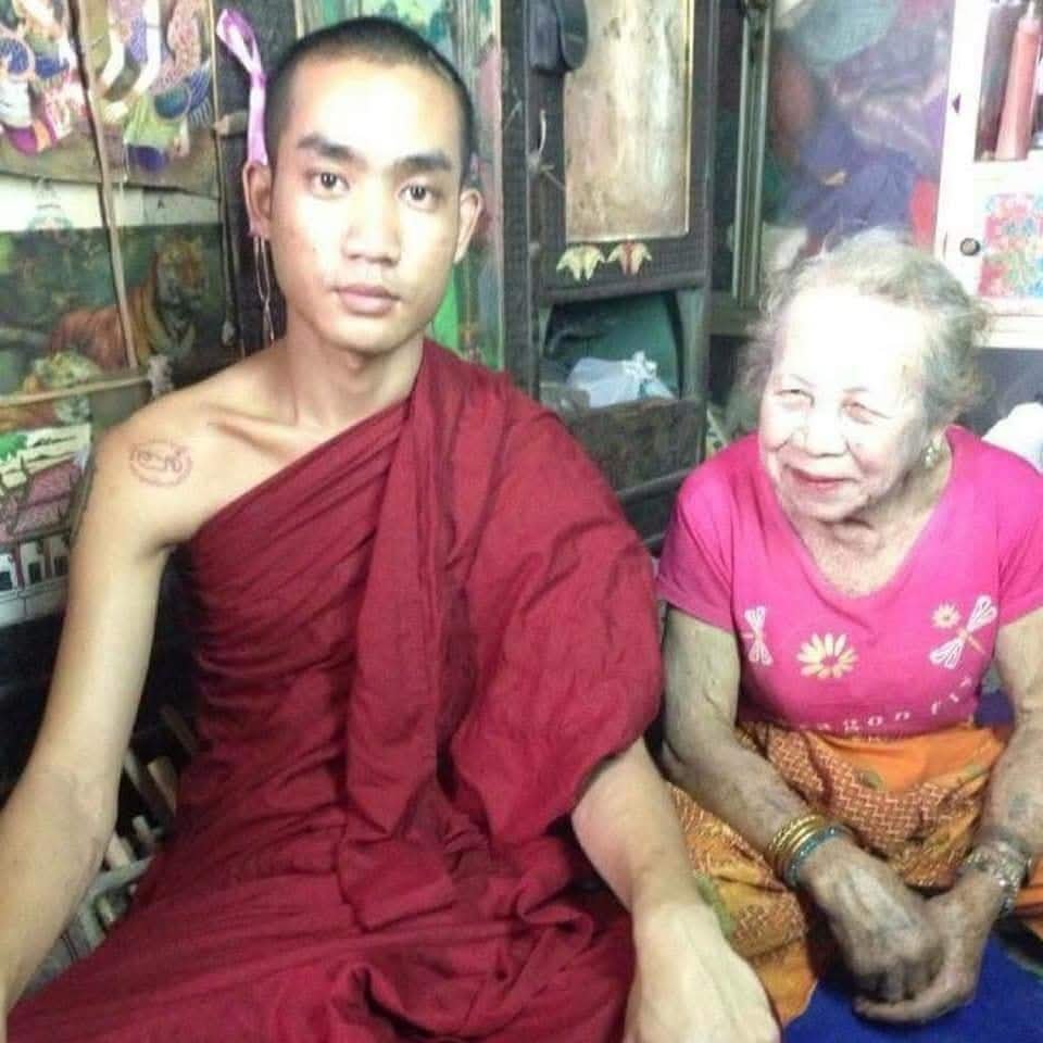 Historical photograph of a young Ajarn Tay in maroon robes seated beside Por Sala Tan in her samnak.