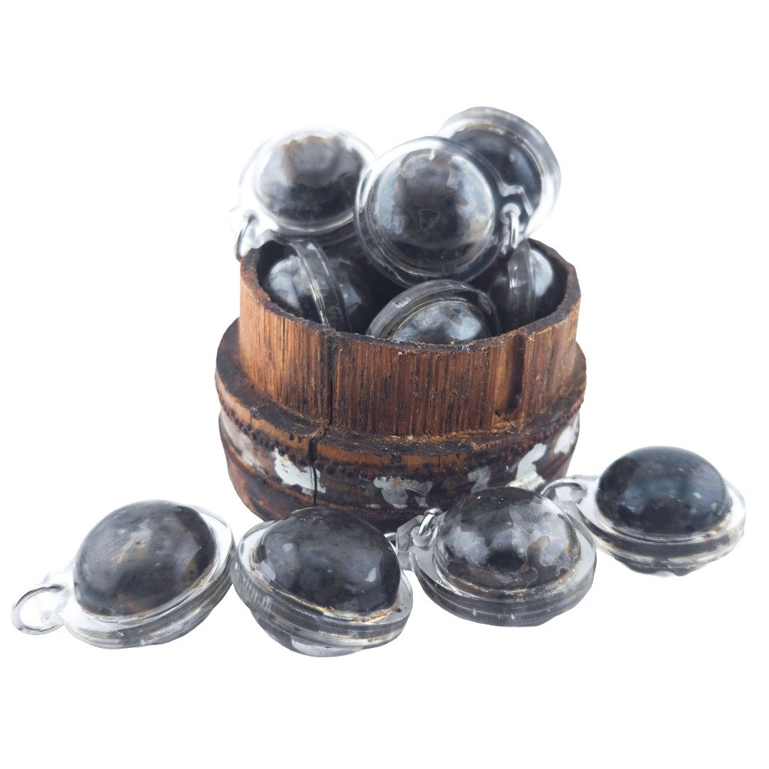 Group of Pure Hakom Wax Luk Om displayed inside and around a wooden container, showing the dark wax and clear pendant casings.