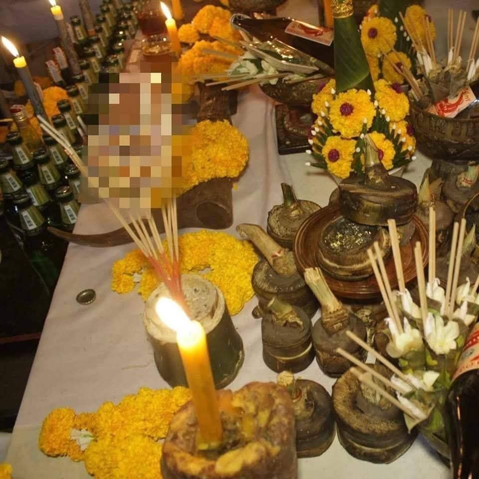 Close-up of a Hakom ritual altar with burning candles, incense, flower garlands and ritual objects arranged for blessing ceremonies.