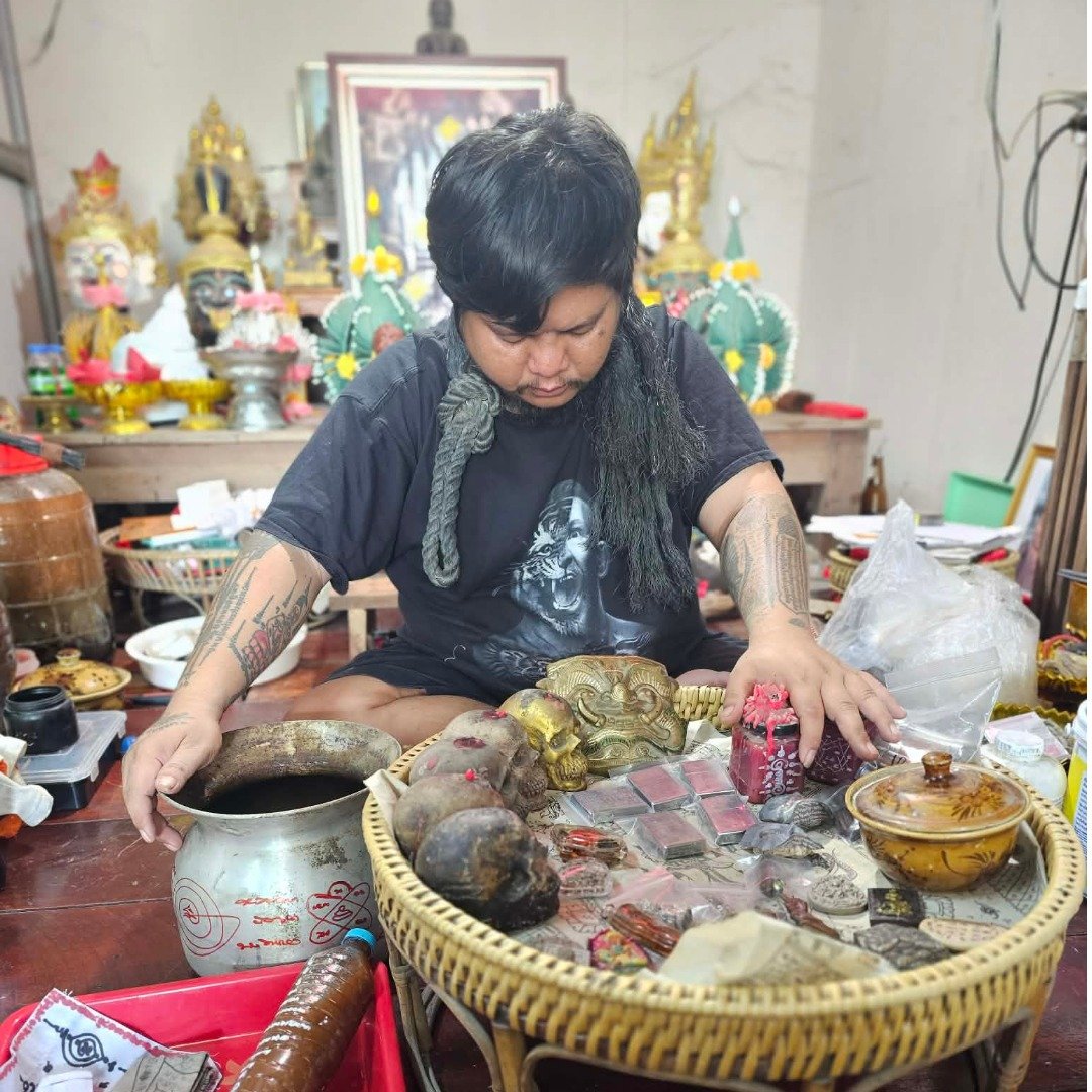 Ajarn Kitkamo conducting a blessing session for multiple amulets and ritual objects, with his Prai Command Whip resting over his shoulder.